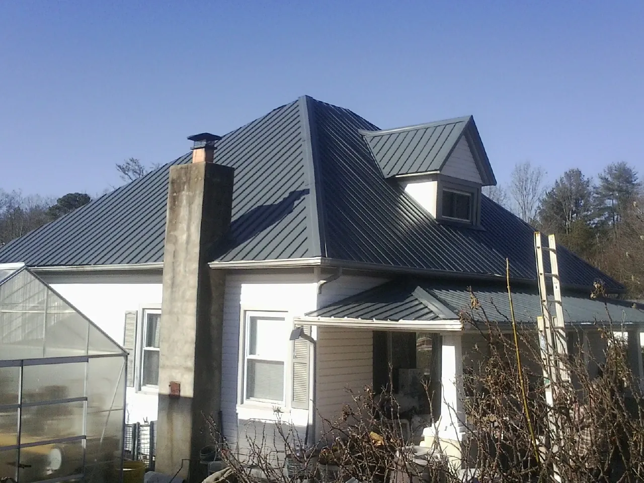 Dark blue standing seam metal roof on a white farmhouse with dormer — Slate & Tile Roof Repair by Roofing Brothers in Talmage