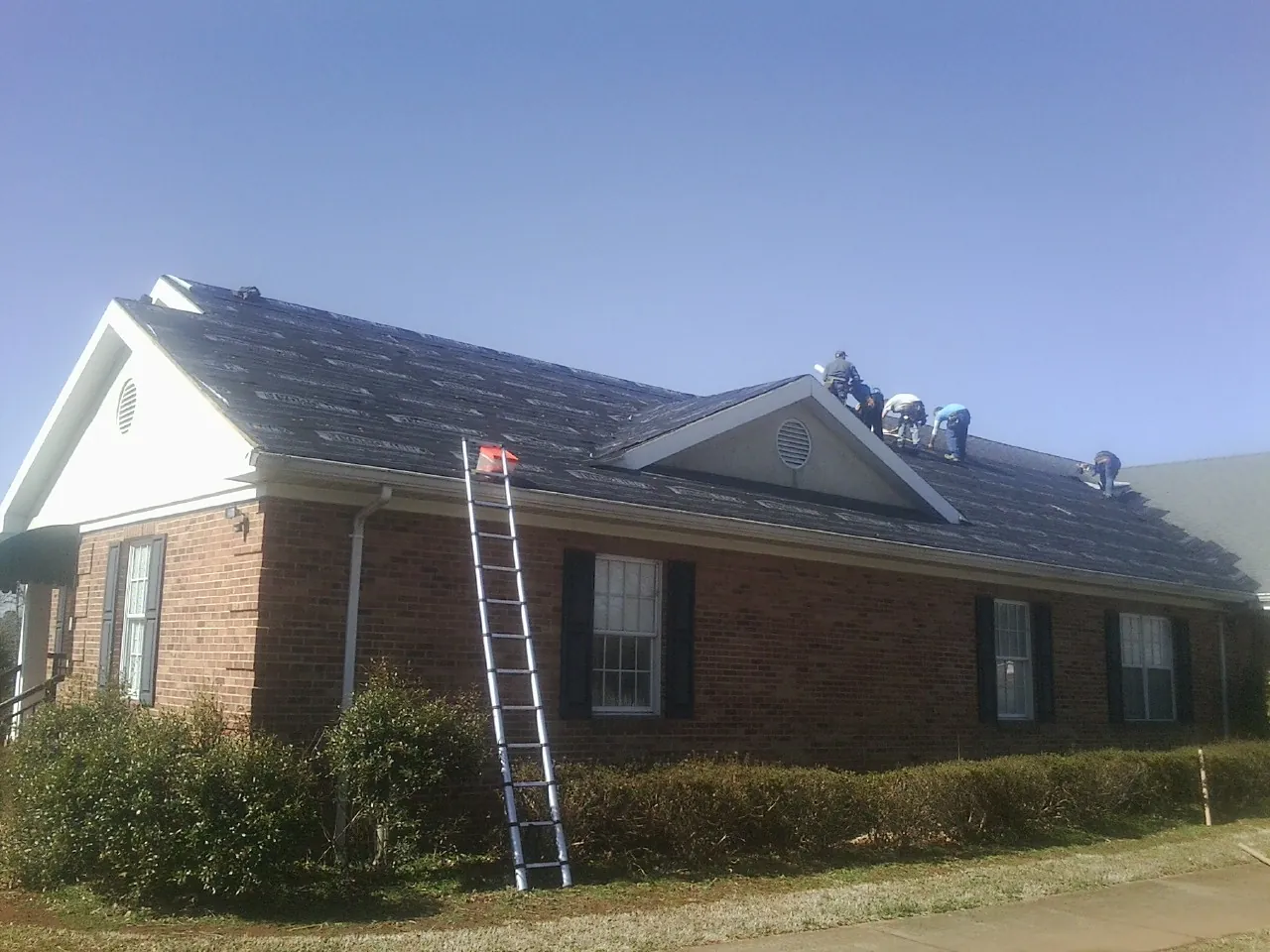 Crew tearing shingles off a brick ranch roof with a ladder set — Metal Roof Repair work by our crew in Talmage