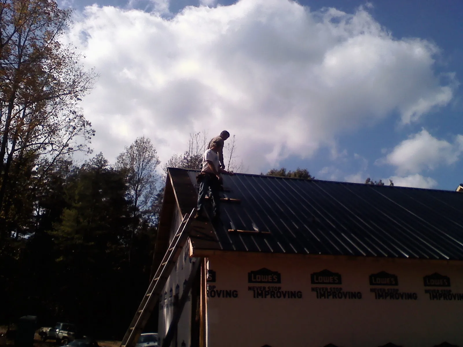 Roofer fastening dark metal panels high against a cloudy sky, from a Roof Inspection job in Talmage